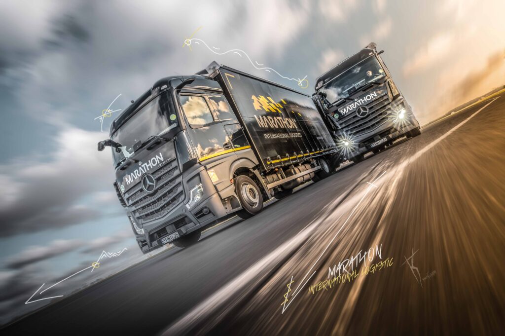 Dwie eleganckie ciężarówki firmy Marathon International Logistic pędzą obok siebie autostradą, a rozmycie ruchu podkreśla potęgę logistyki w akcji.
